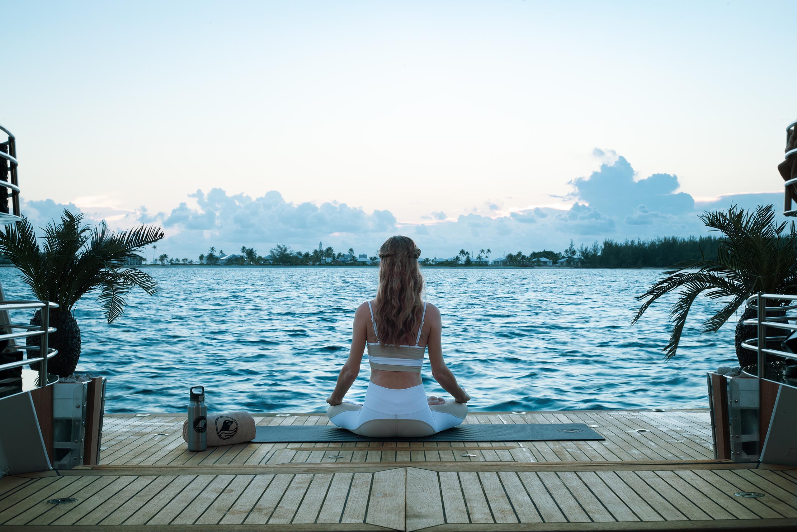 Woman doing yoga at sunrise from on swim platform of superyacht, looking out at sea