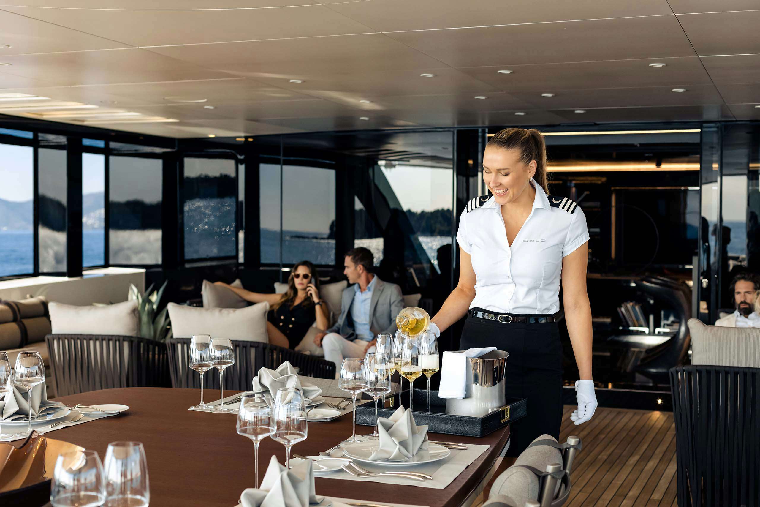 Superyacht stewardess serving wine to charter guests on aft deck