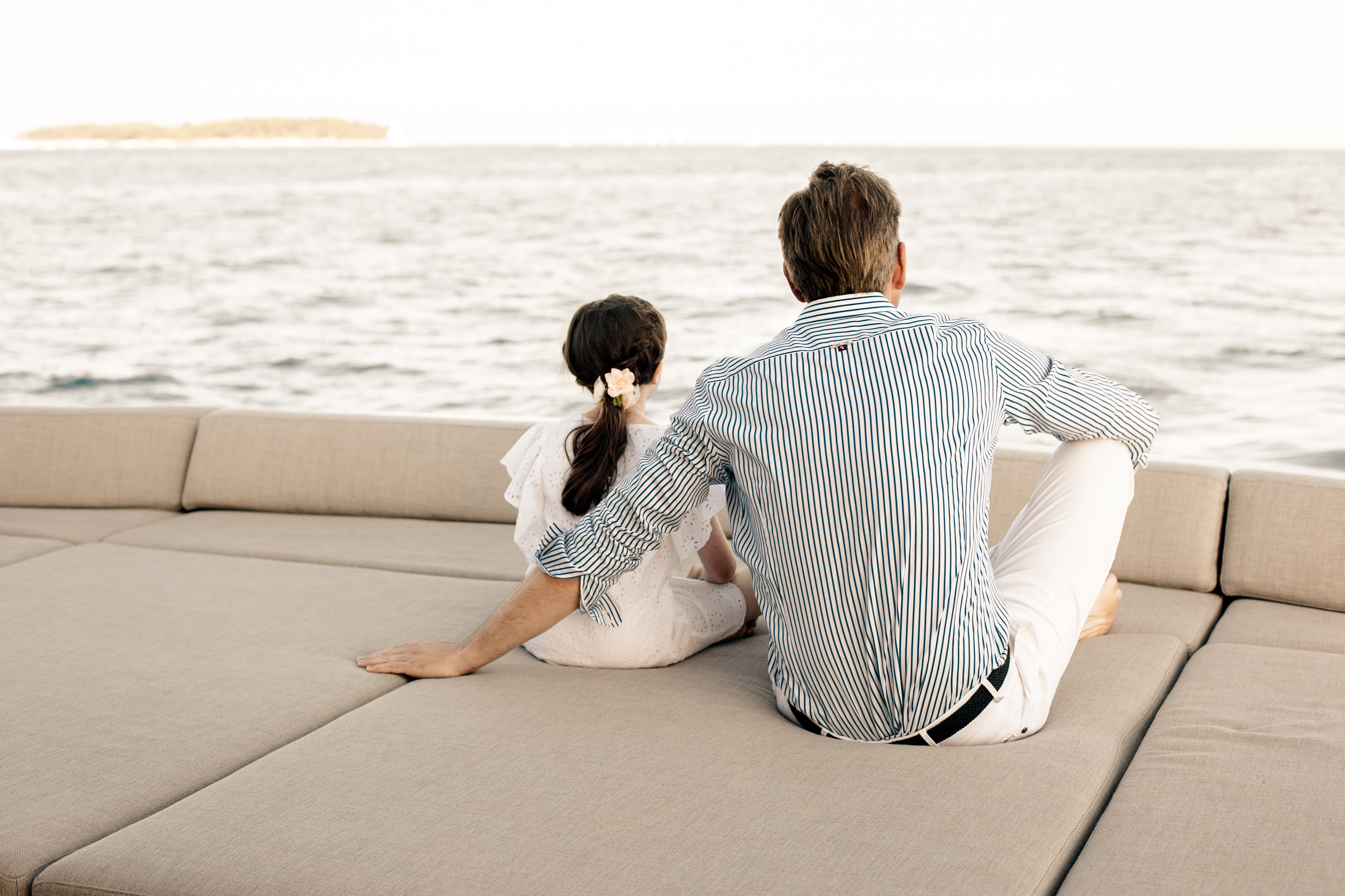 Father and daughter sitting on sun pads on board a luxury yacht looking at the horizon