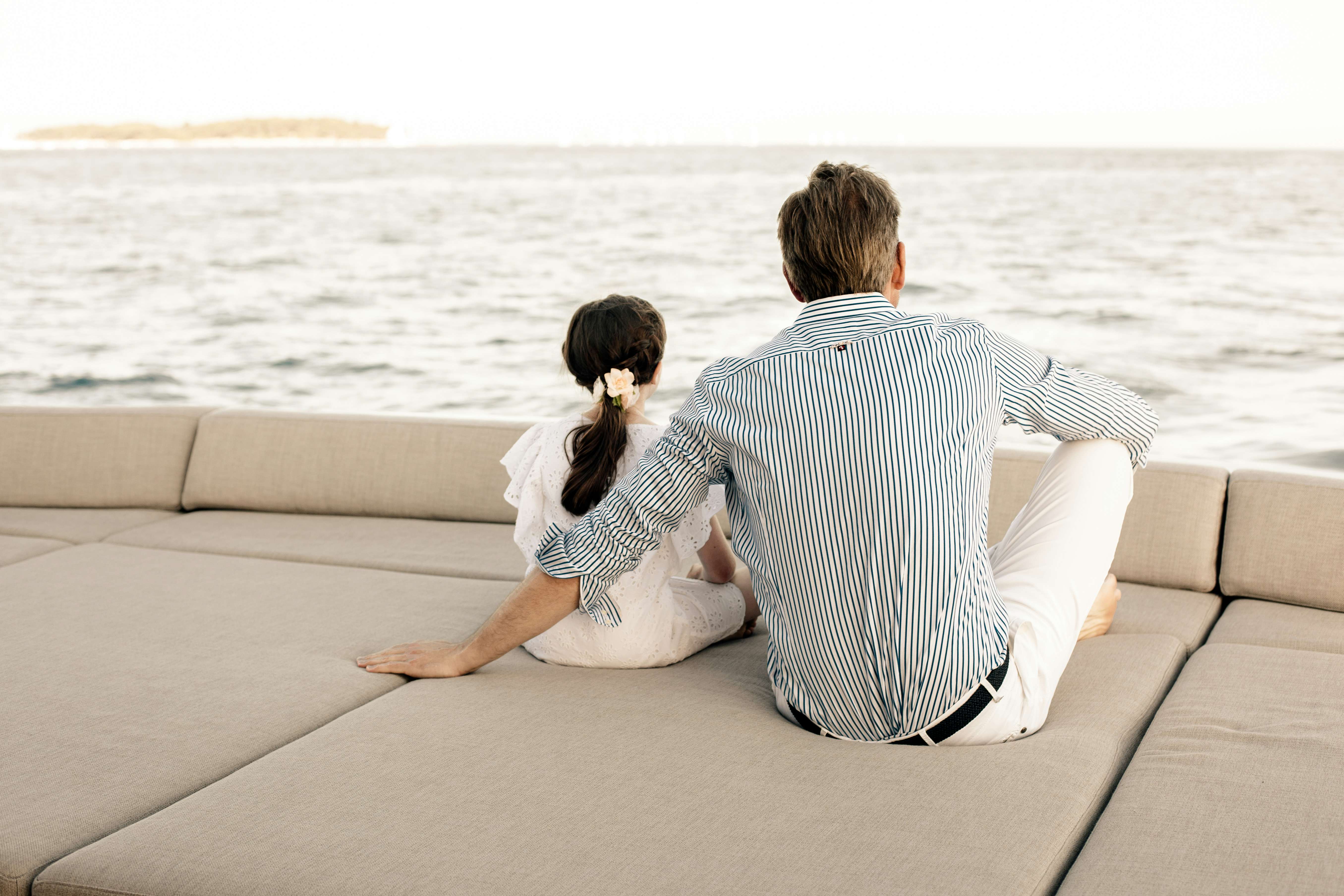 Father and daughter sitting on sun pads on board a luxury yacht looking at the horizon