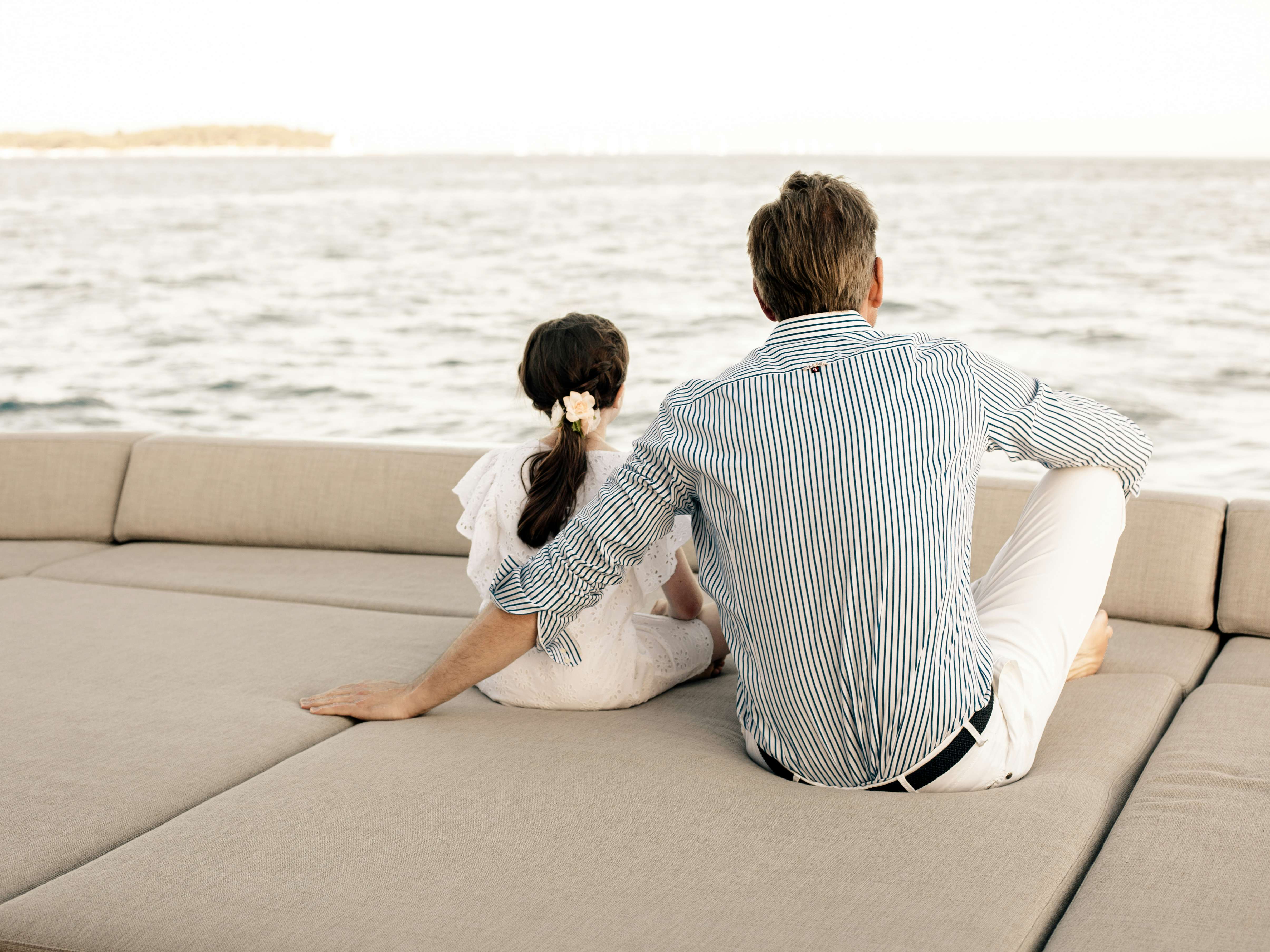 Father and daughter sitting on sun pads on board a luxury yacht looking at the horizon