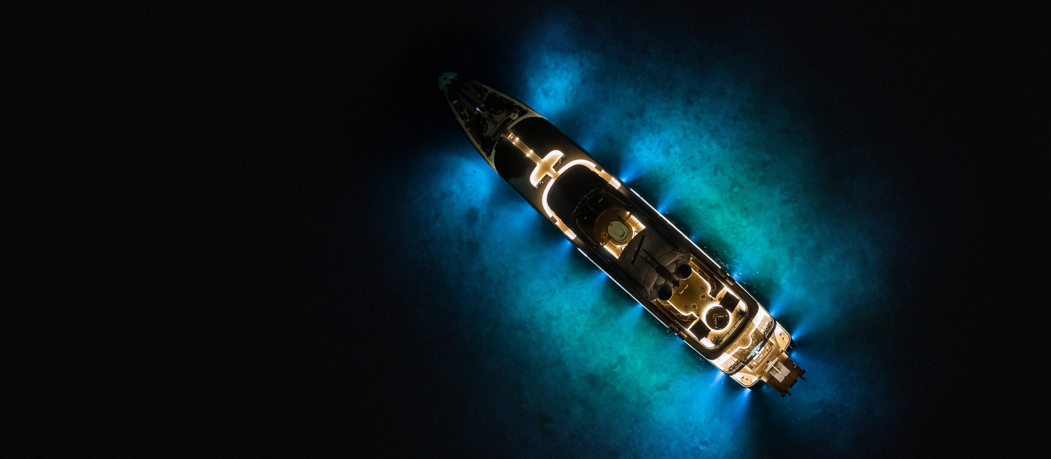 Bird's eye of superyacht anchored at night illuminating the sea bed with her underwater lights