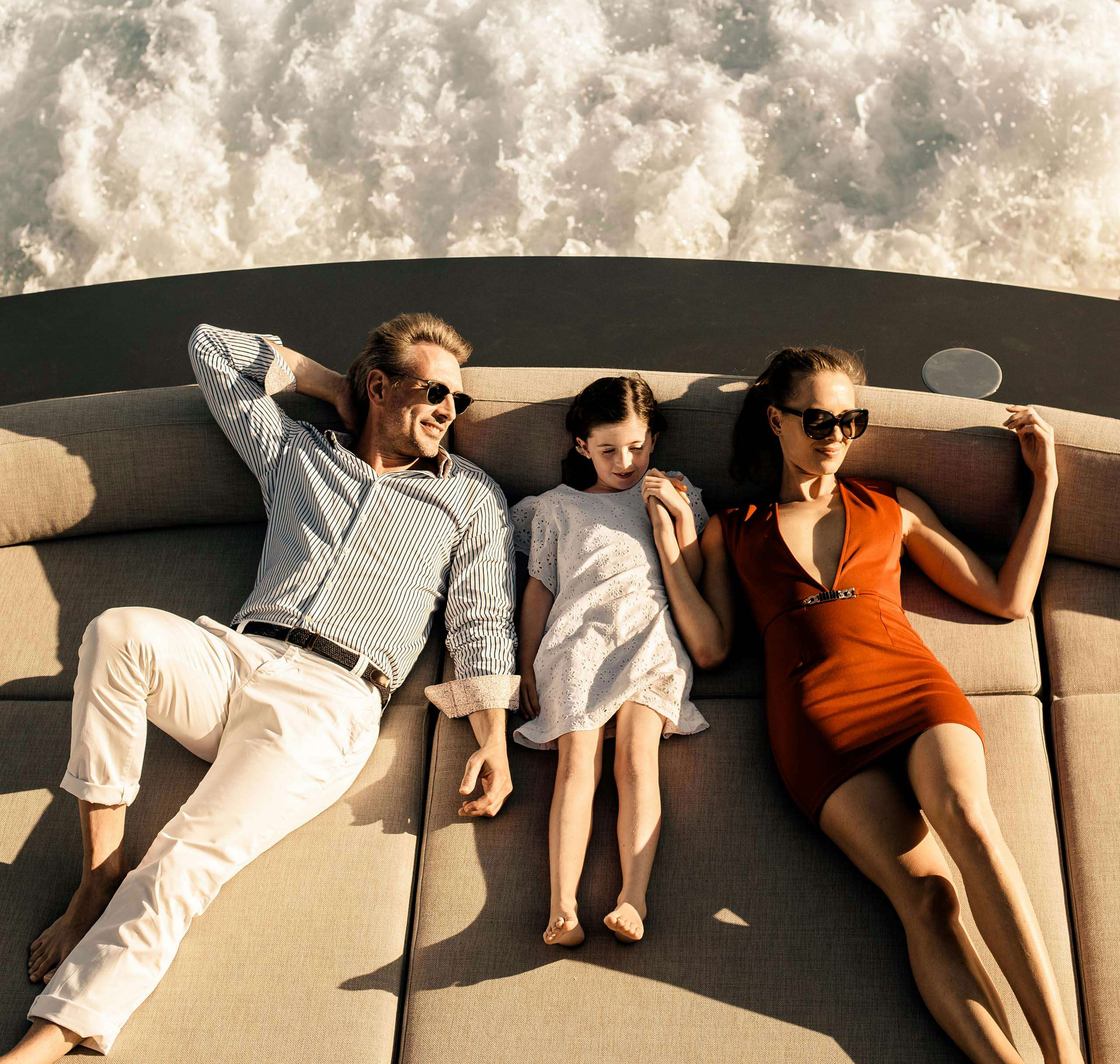 Couple and child relaxing on sun pads on board superyacht while navigating