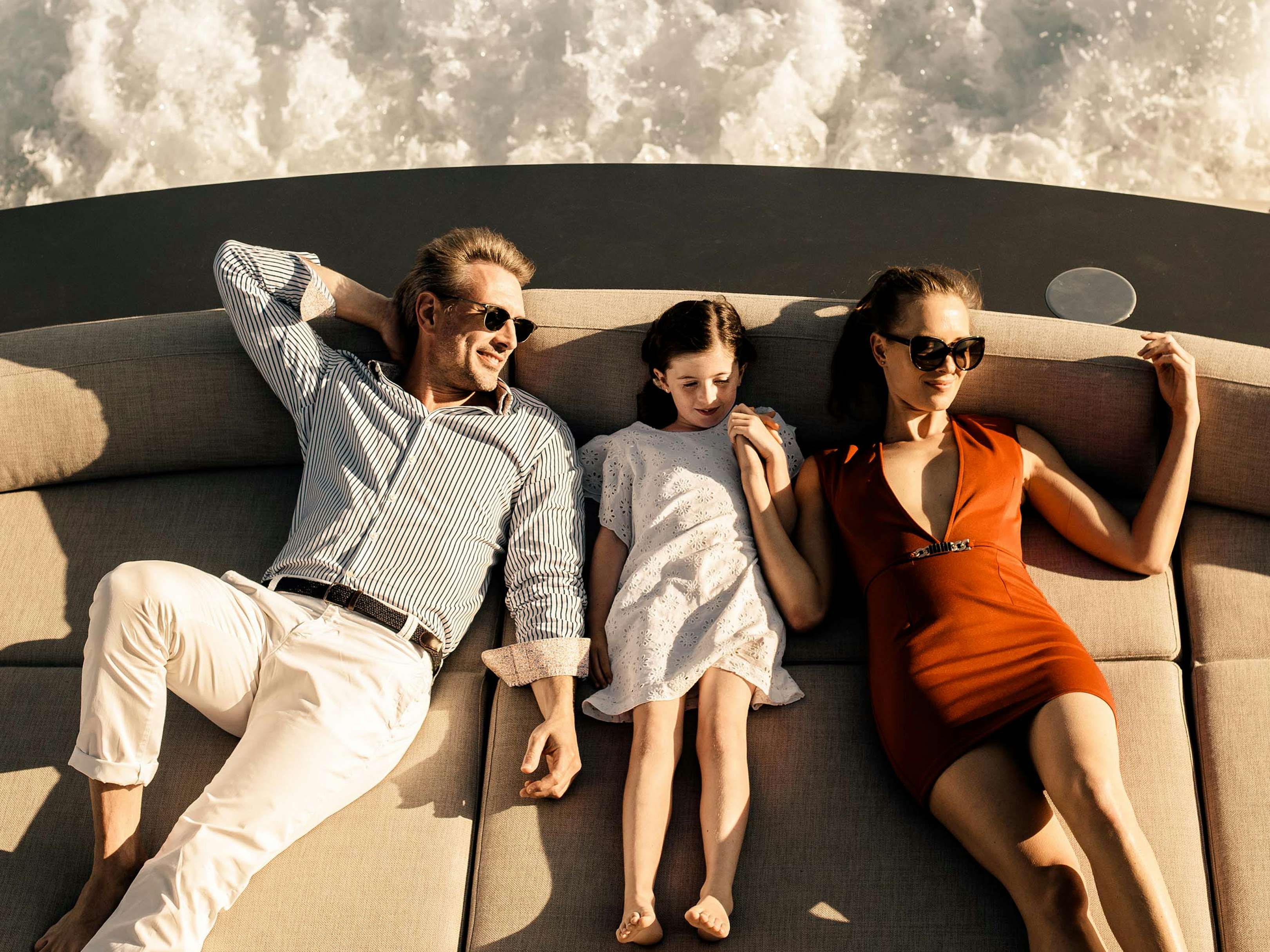 Couple and child relaxing on sun pads on board superyacht while navigating