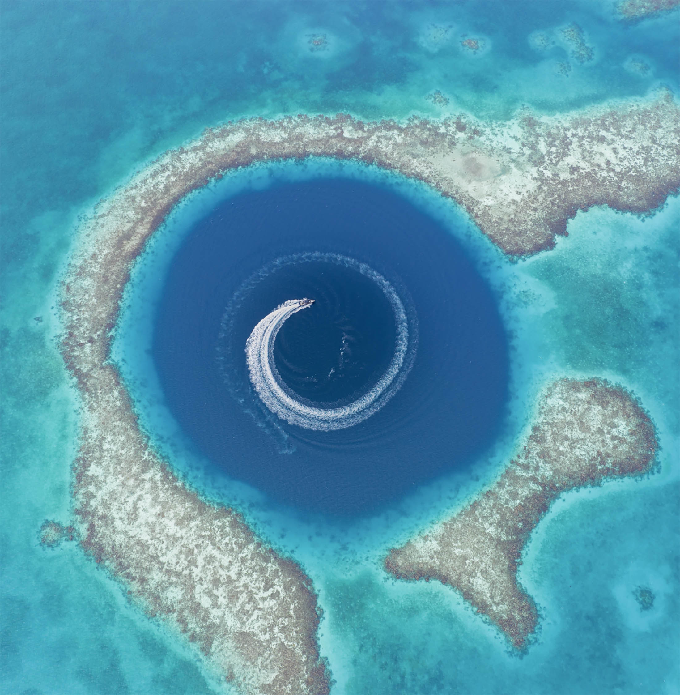 Aerial view of yacht circling inside a deep blue hole in the ocean