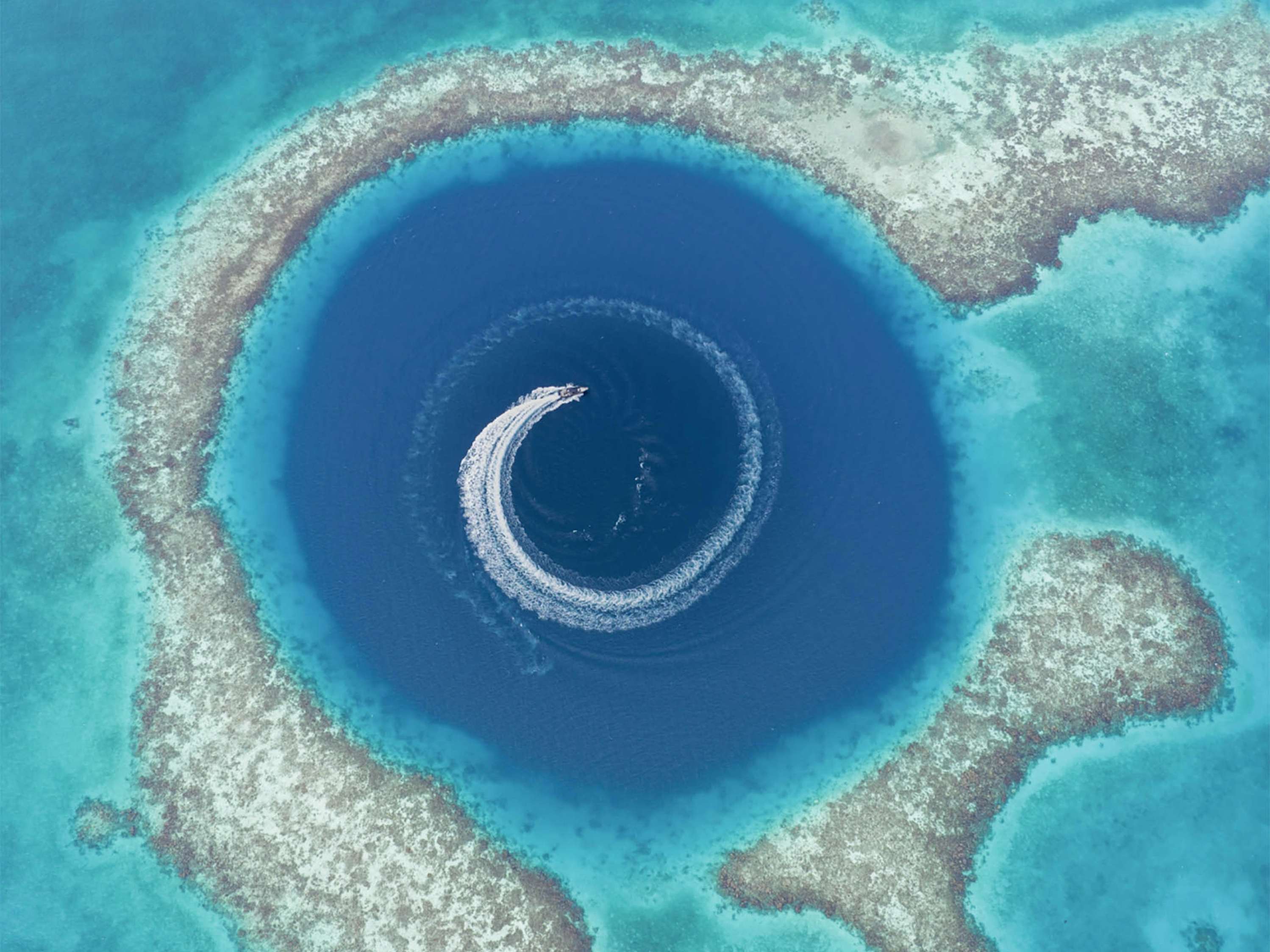 Aerial view of yacht circling inside a deep blue hole in the ocean