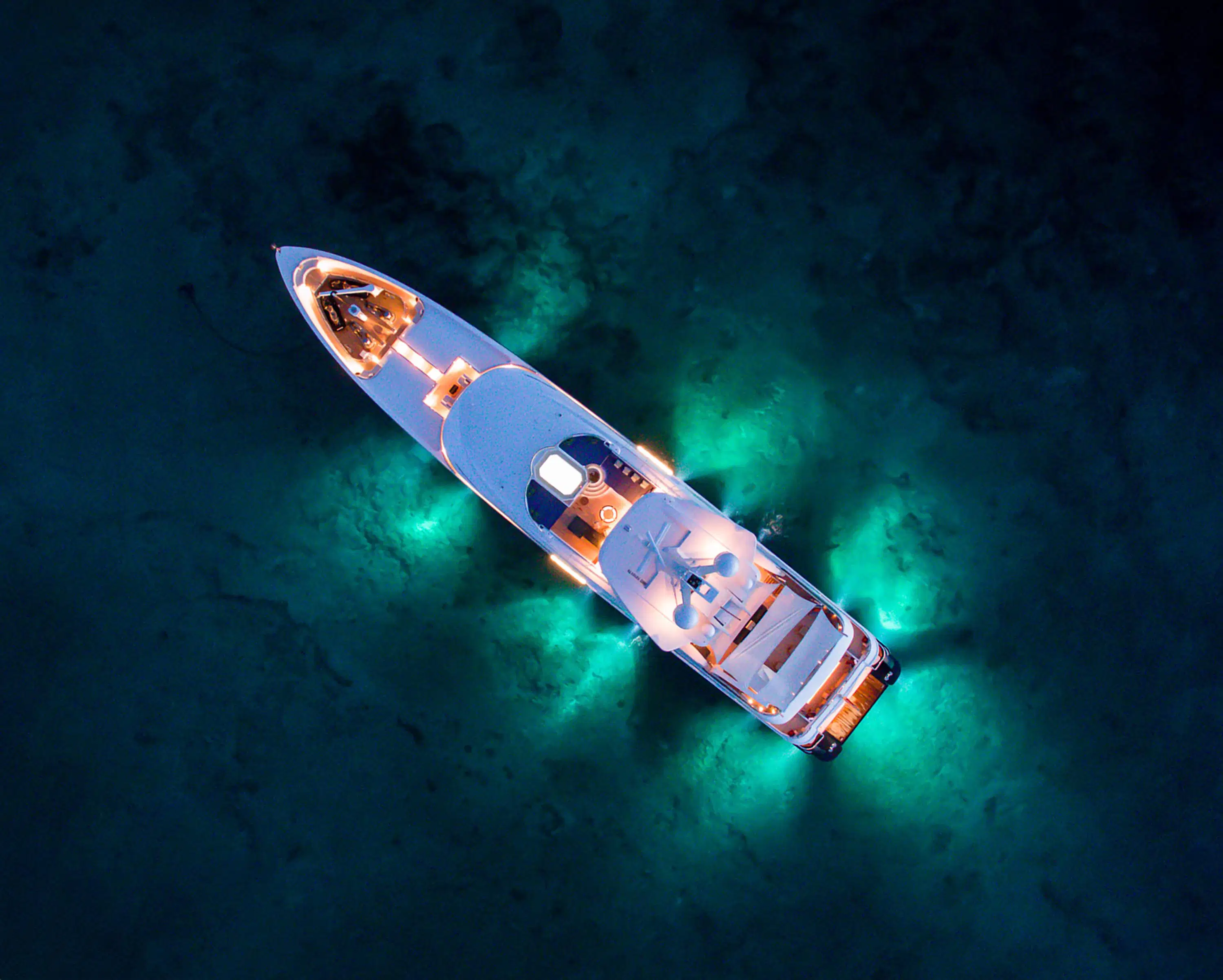 Aerial view of yacht anchored at night with underwater lights glowing